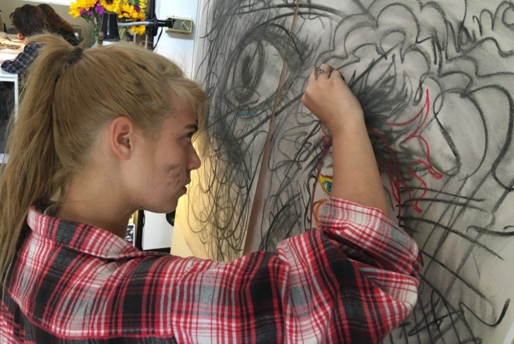 girl scribbling with charcoal on a large canvas